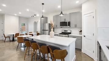 Una cocina moderna con una isla central, taburetes de bar, electrodomésticos de acero inoxidable e iluminación colgante.