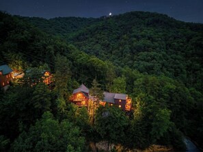 Ein bewaldetes Gebiet mit mehreren Gebäuden, darunter eine Hütte mit Balkon und ein größeres Haus mit zahlreichen Fenstern.