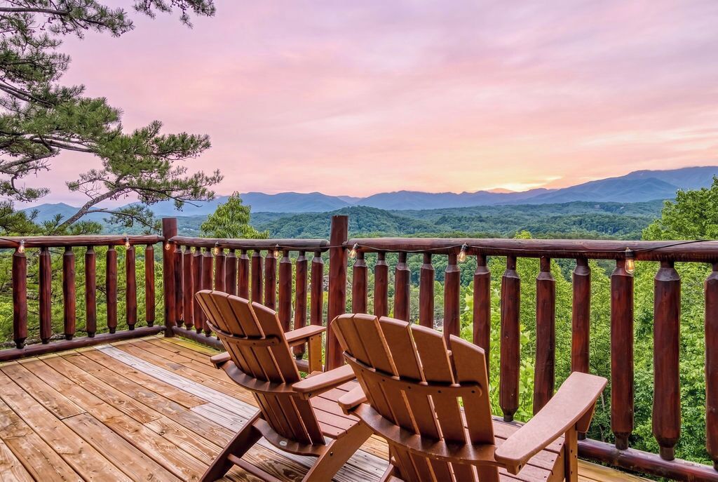 A wooden deck with Adirondack chairs overlooking a mountainous landscape.