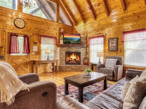 Ein Blockhaus-Interieur mit Kamin, Holzwänden, einer Uhr und einer gemütlichen Sitzecke.