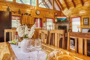 Ein Holzhütten-Innenraum mit Esstisch, Stühlen, Kamin und einer Wanduhr.