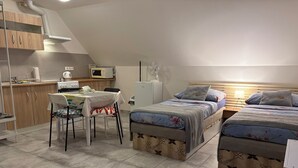 A compact room with a kitchenette, a dining table with chairs, and two beds with floral bedding.