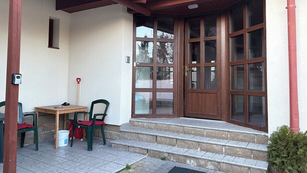 A building entrance with a wooden door, steps, a small table, and chairs.