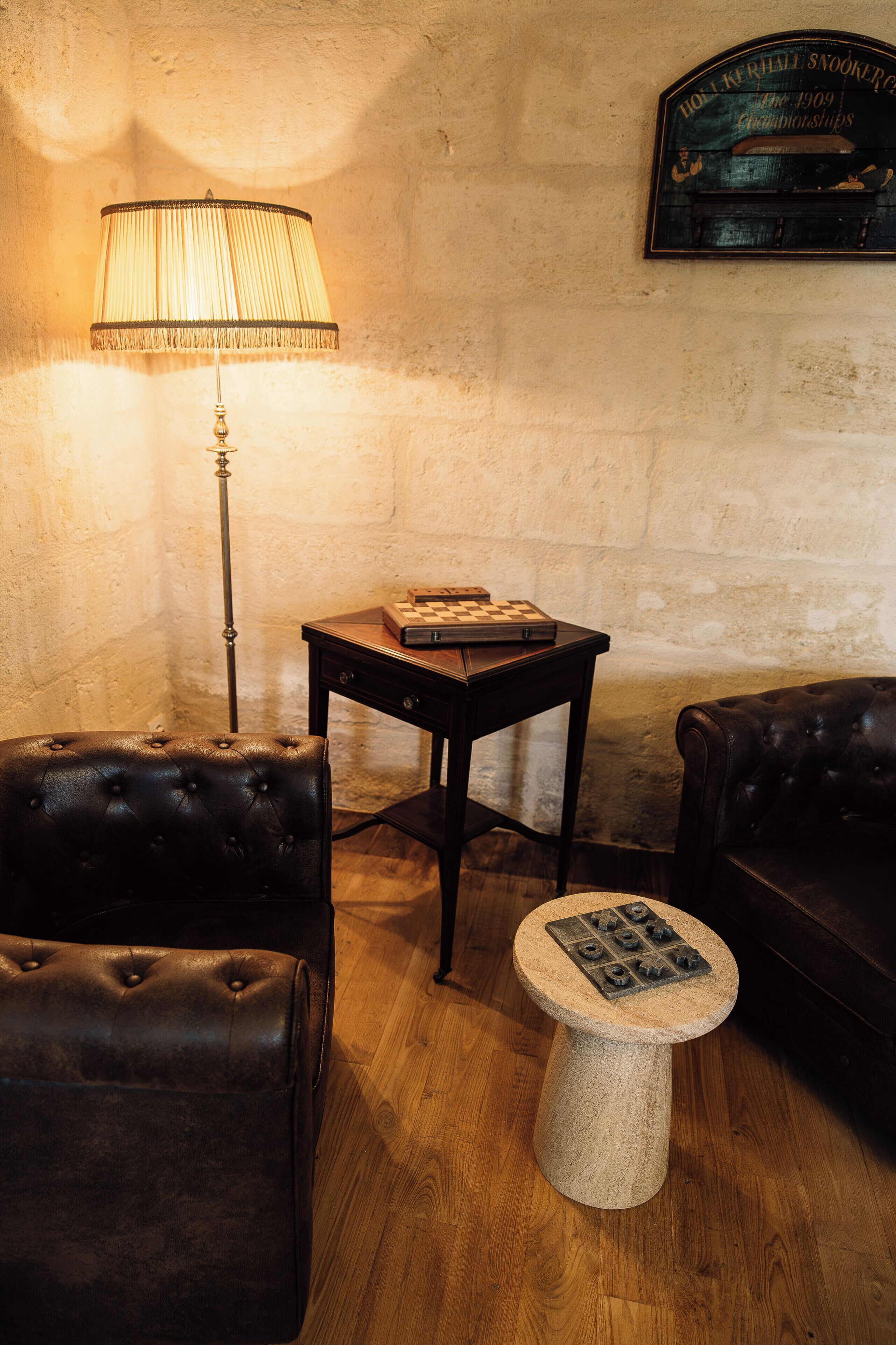 Una habitación con dos sillones de cuero, una pequeña mesa con un tablero de ajedrez, una lámpara y un letrero en la pared.