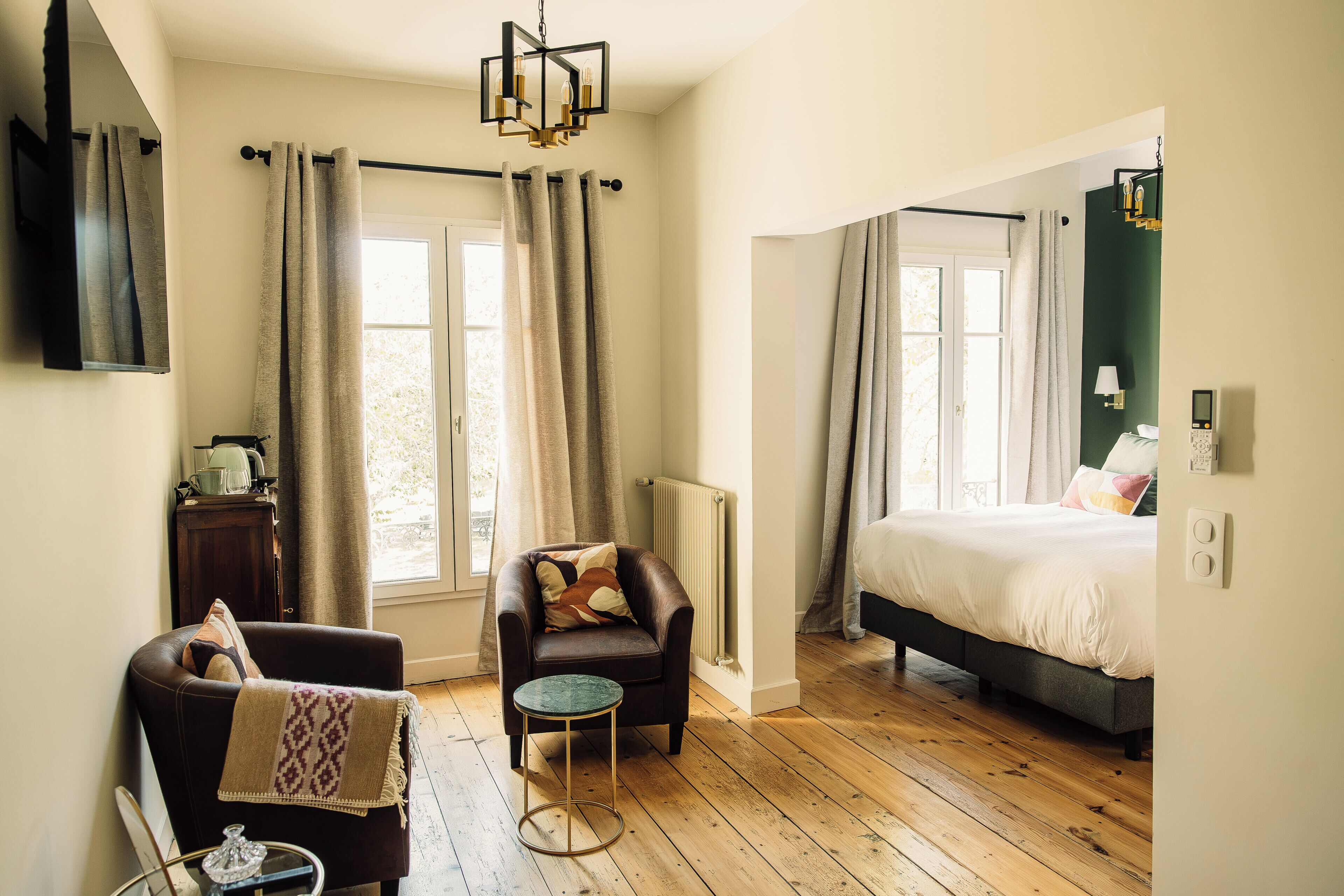 A bedroom with a bed, a chair, a small table, a radiator, and a window.