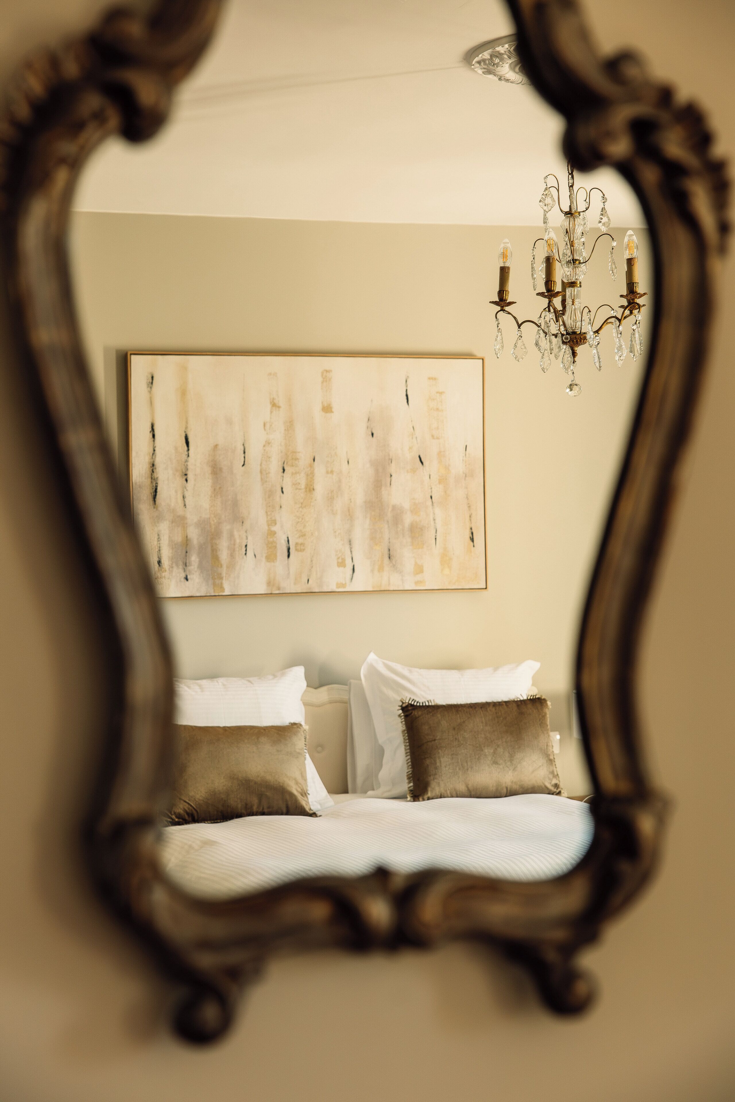 Un dormitorio con cama, almohadas, una araña de cristal y un cuadro abstracto grande en la pared.