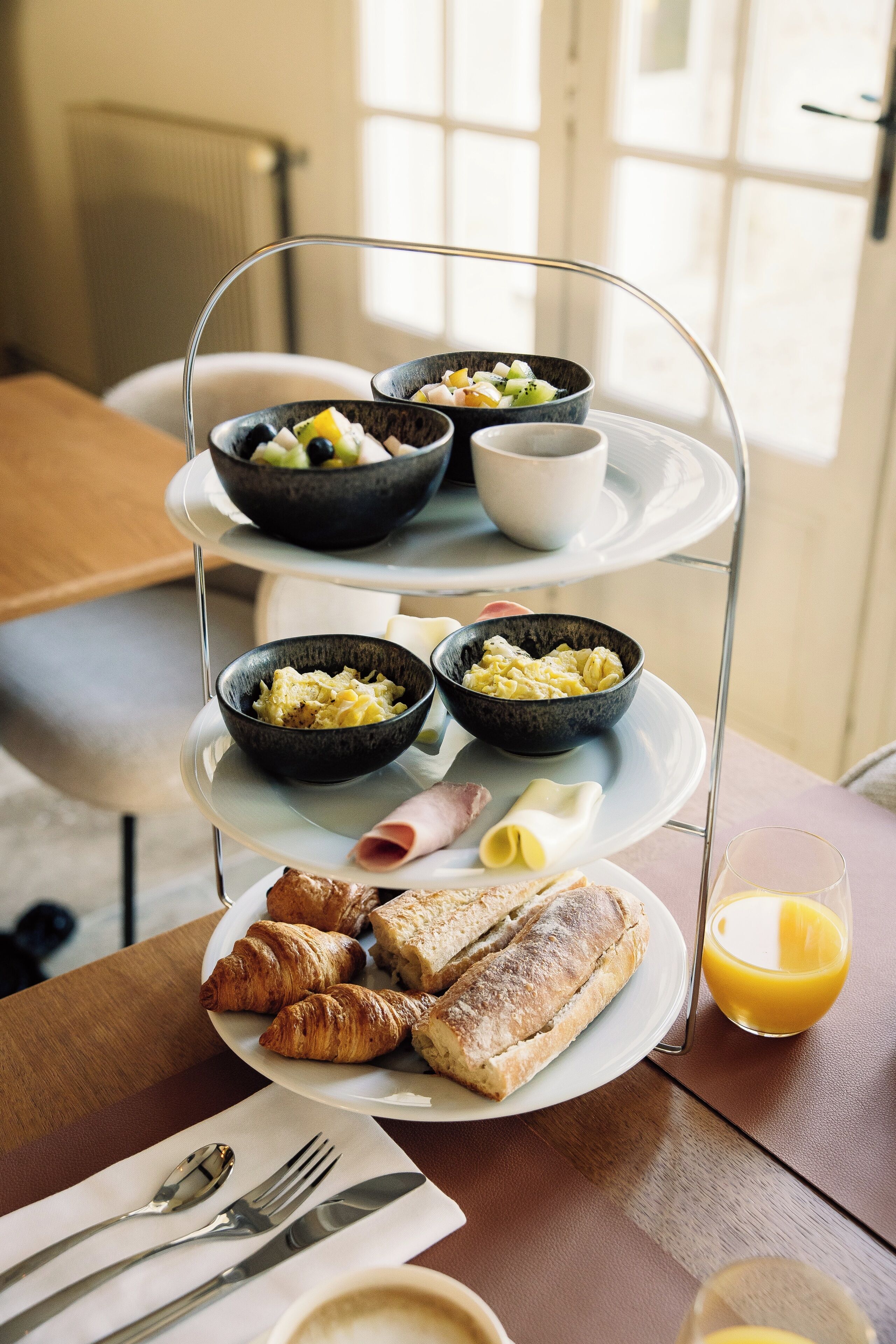 Bandeja de desayuno con croissants, huevos revueltos y un vaso de jugo de naranja.