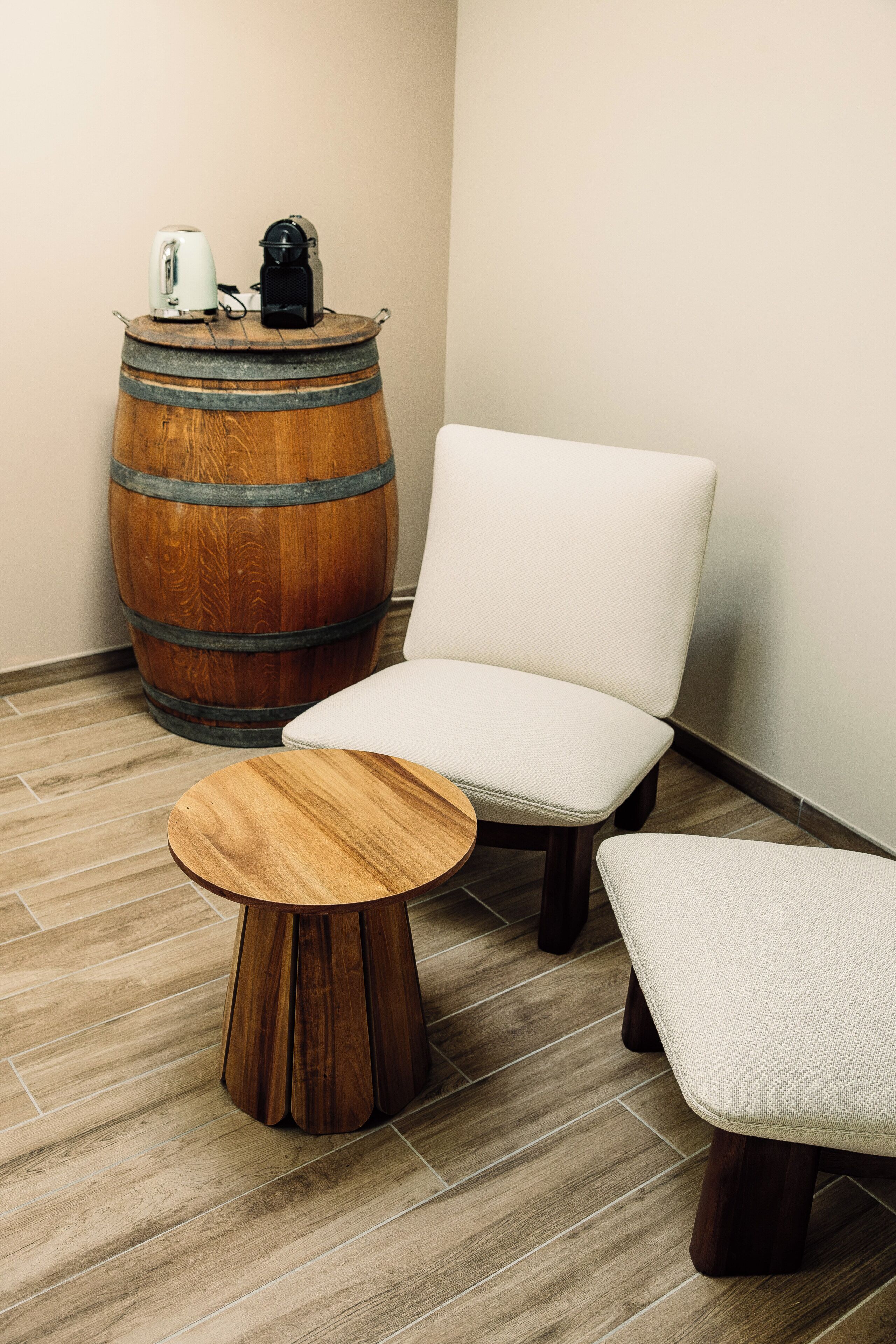 Een kamer met een houten vat, een witte fauteuil en een ronde houten tafel.