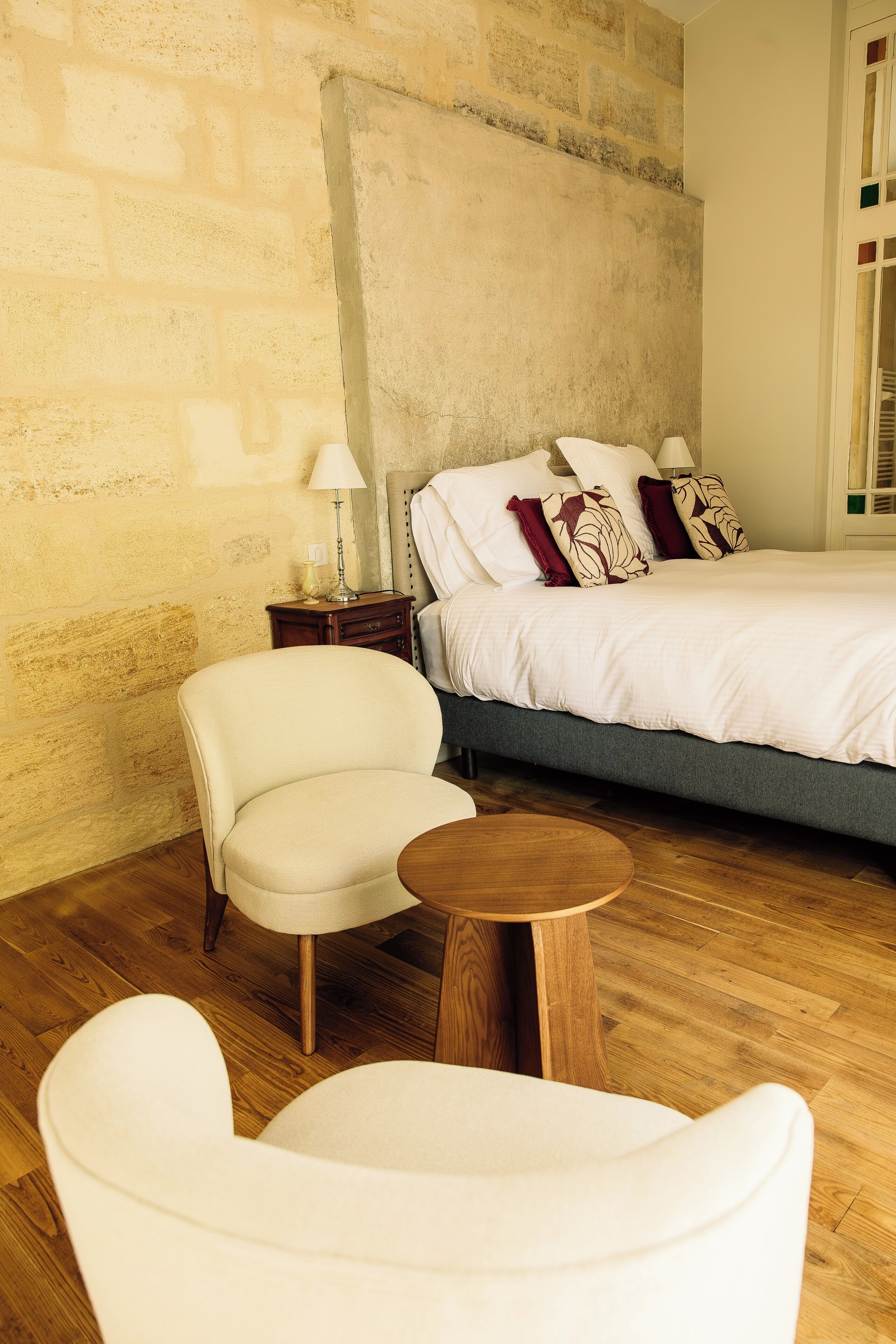 Un dormitorio con cama, dos sillas, una mesita de noche y una lámpara.