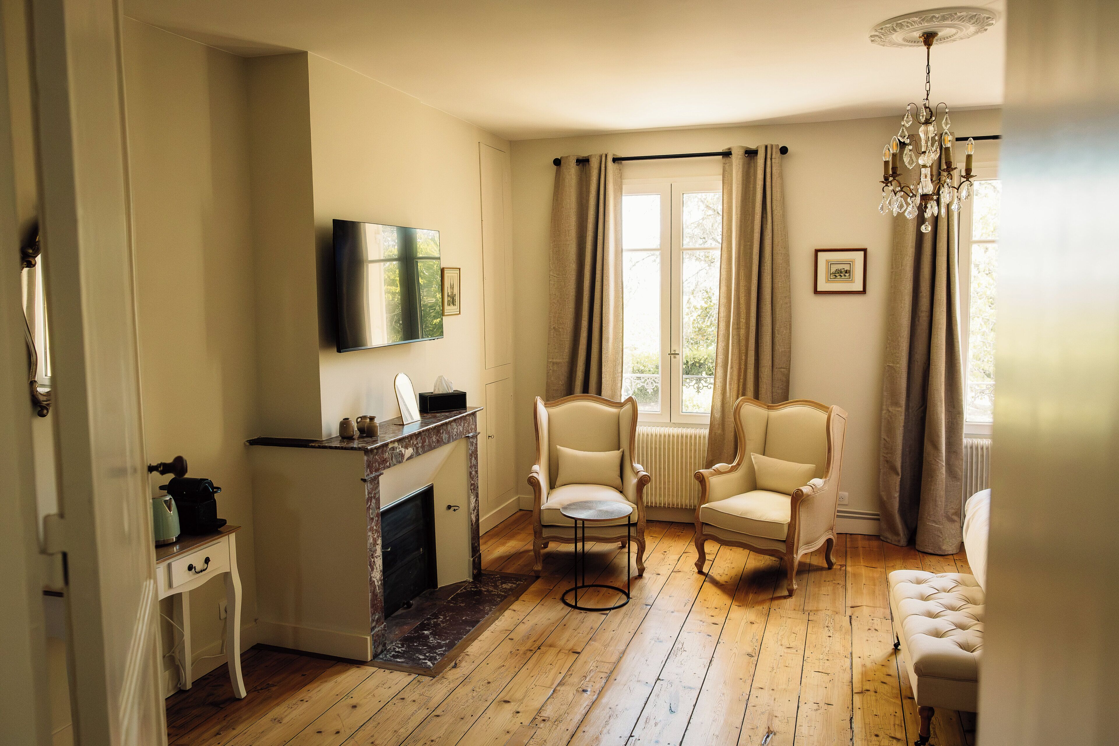 Een kamer met een open haard, twee fauteuils, een televisietoestel en een kroonluchter.