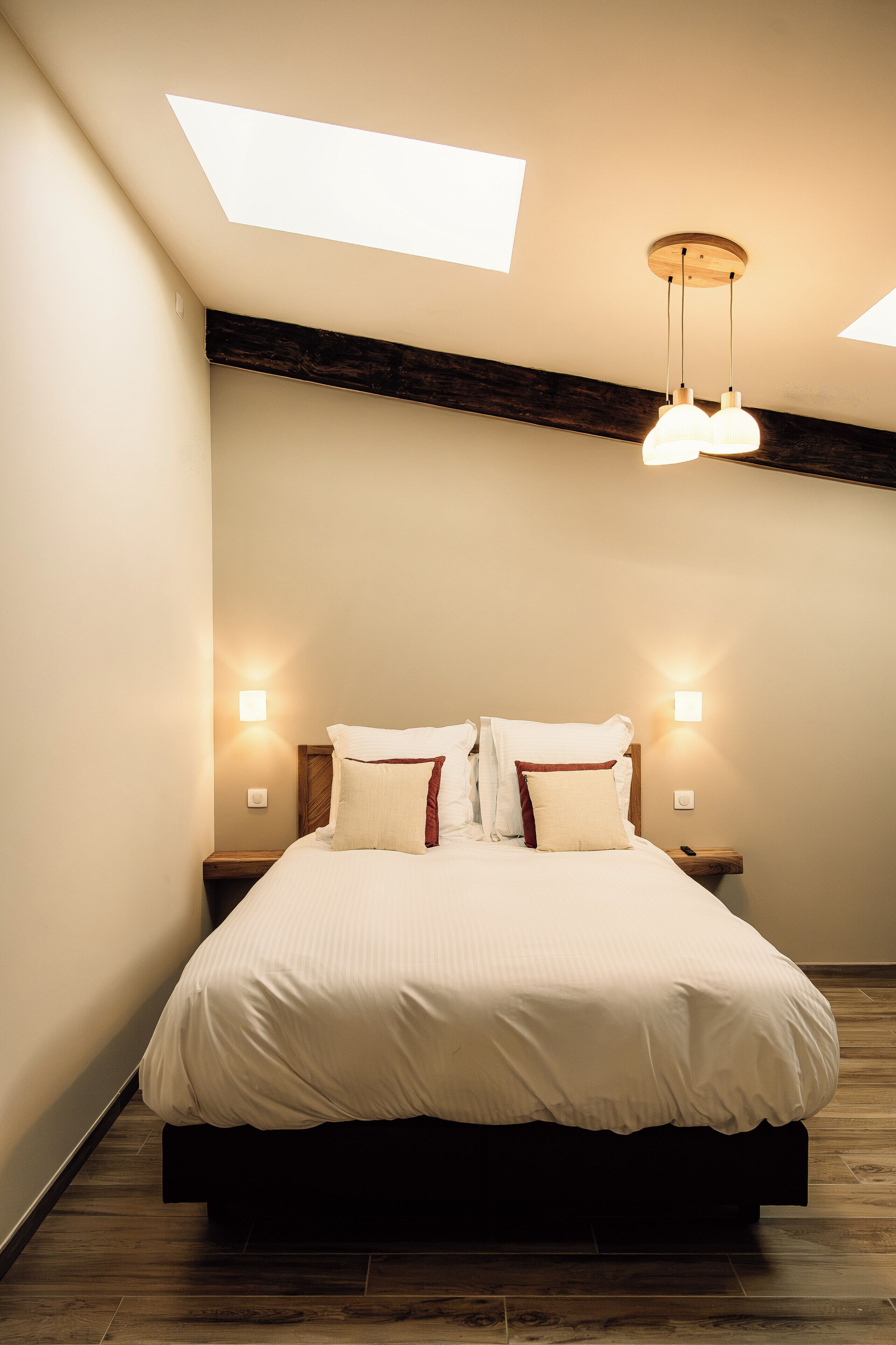 Une chambre à coucher avec un grand lit, une tête de lit en bois, deux lampes de chevet et une lucarne.