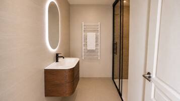 A modern bathroom with a vanity, a mirror with a light, and a towel rack.