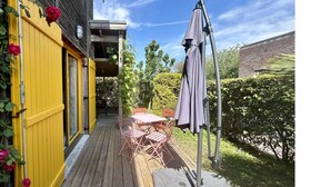 En träveranda med en gul dörr, ett bord med stolar och ett lila parasoll.