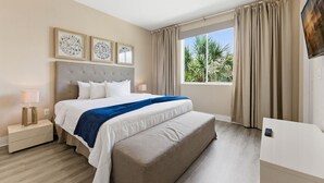 A hotel room with a bed, bedside tables, a TV, and a window with curtains. - Designer 4BR Getaway, Sleek Laminate Floors (Kissimmee)