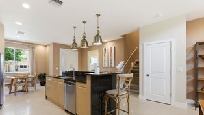 A modern kitchen with a central island, pendant lighting, a dining area with chairs, and a staircase. - Designer 4BR Getaway, Sleek Laminate Floors (Kissimmee)