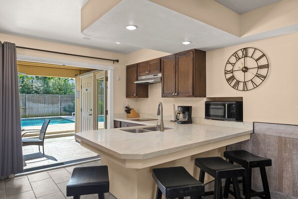 A kitchen with a large island, a clock, and a view of a backyard with a pool.