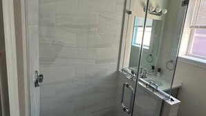 Eine gläserne Dusche mit gefliestem Wandbereich, einem sichtbaren Abfluss und einer Glastür mit Griff.