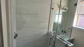 A glass-enclosed shower with a tiled wall, a visible drain, and a glass door with a handle.