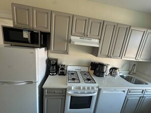 Eine kompakte Küche mit Mikrowelle, Kaffeemaschine, Herd, Backofen und Geschirrspüler.