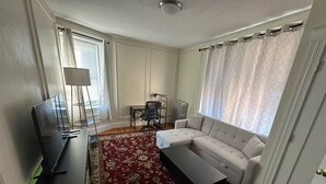 Ein Wohnzimmer mit einer Couch, einem Couchtisch, einem Fernseher, einer Lampe, einem Sessel und einem gemusterten Teppich.
