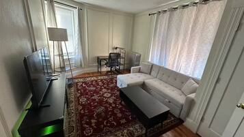 A living room with a sofa, a coffee table, a TV, a lamp, a chair, and a patterned rug.