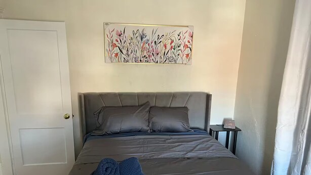 Ein Schlafzimmer mit Bett, Kissen, einem Nachttisch, einer Uhr und einem Bild an der Wand.