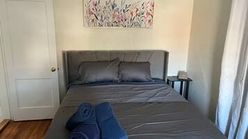 A bedroom with a bed, pillows, a nightstand, a clock, and a painting on the wall.