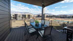 Eine überdachte Terrasse mit einem Glastisch und Stühlen, mit Blick auf eine gebirgige Landschaft und Wohnhäuser.