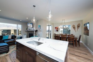 A modern kitchen with a large island, wooden dining table, and pendant lights.