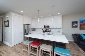 A modern kitchen with white cabinetry, stainless steel appliances, and a central island with stools.