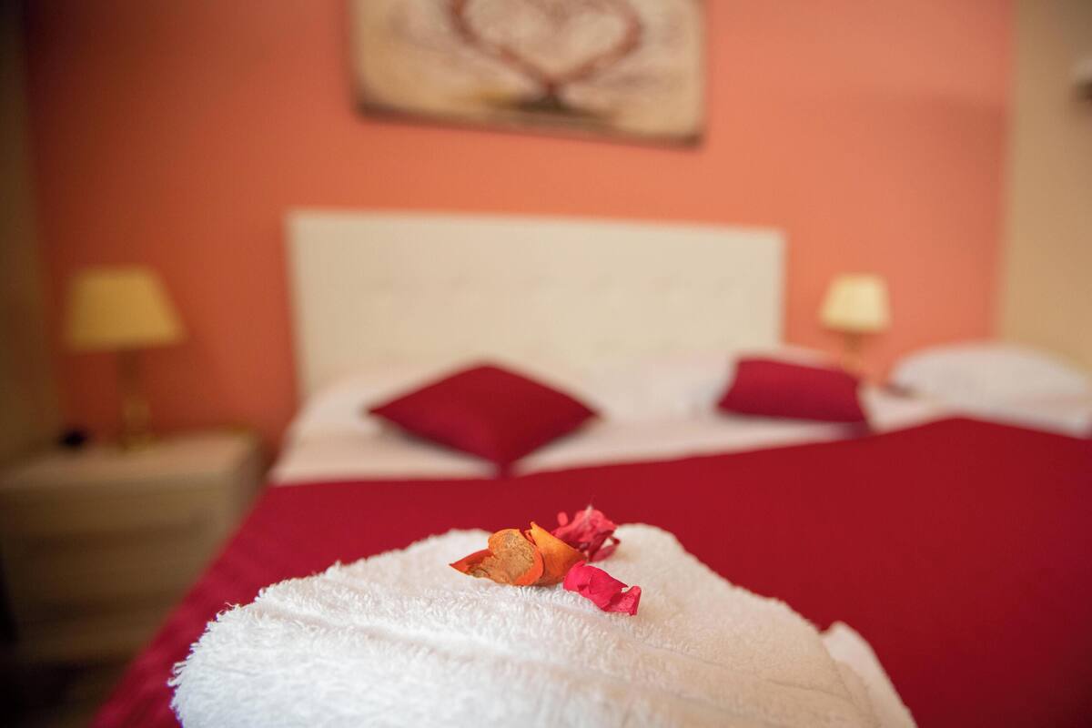 Quarto de hotel com cama, almofadas, toalha branca e manta vermelha.