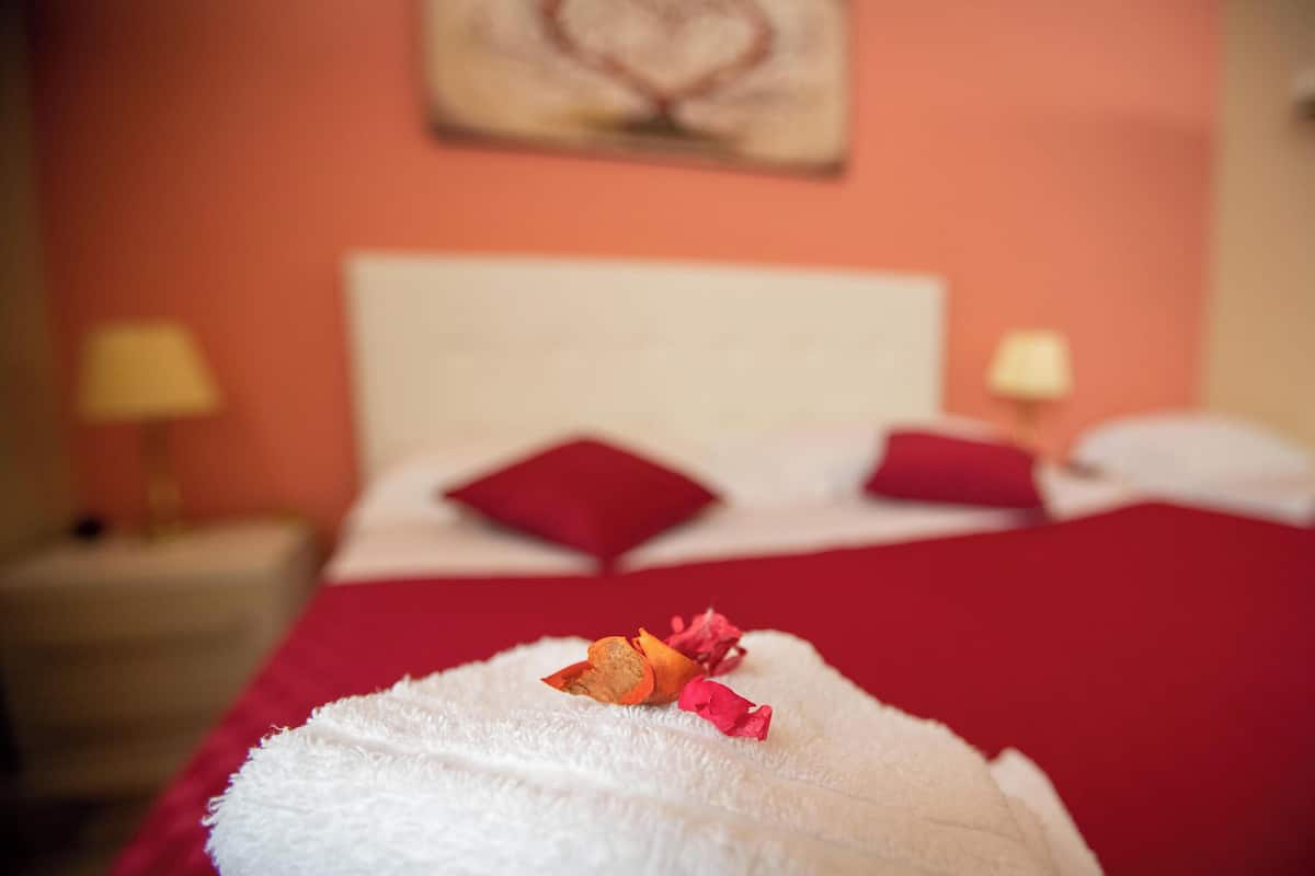 Una habitación de hotel con cama, almohadas, una toalla blanca y una manta roja.