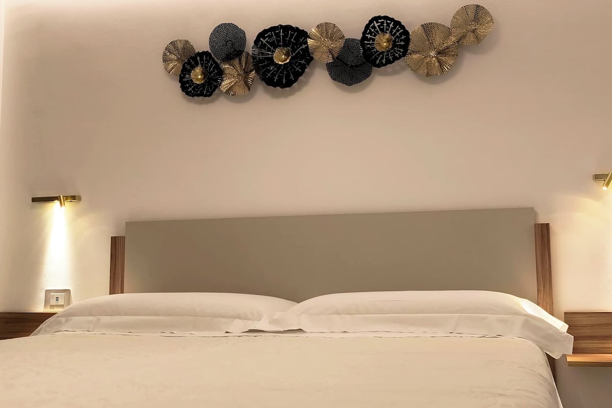 Una habitación de hotel con una cama, dos lámparas fijadas a la pared y un adorno mural.