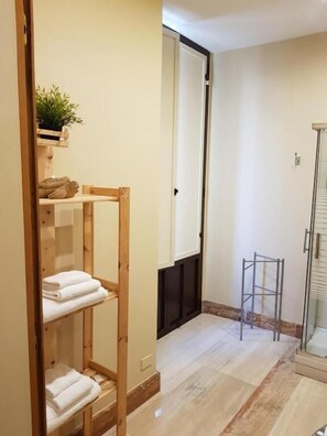 A bathroom with a wooden shelf holding towels, a glass shower enclosure, and a plant on the wall. - B&B Sicily Luxury  (Catania)