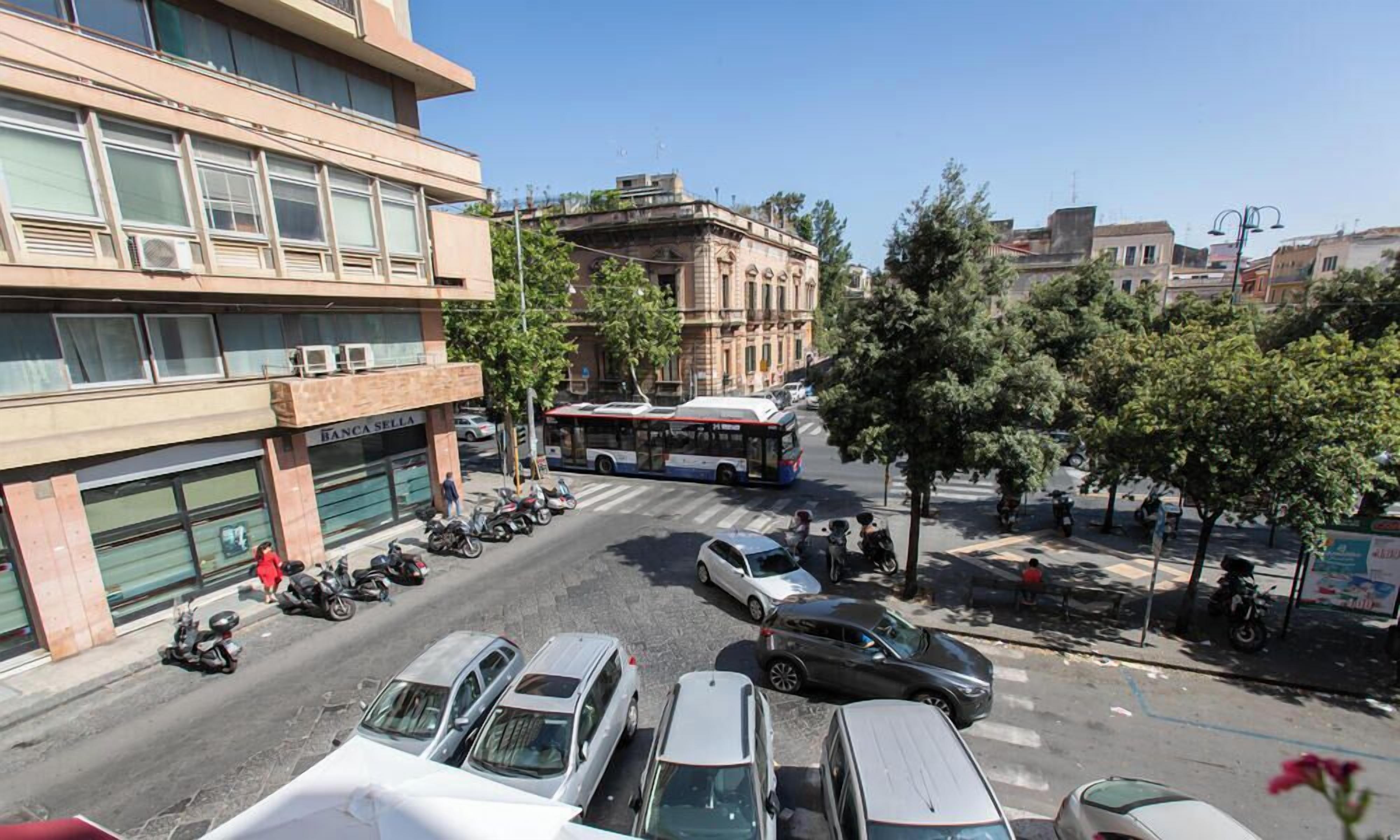 A street view with parked cars, a bus, and a building with a sign reading 'BANCA SERRA'.