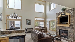 A spacious living area with a stone fireplace, a dining table, and a large window overlooking a scenic view. - Lakefront Luxury Retreat LS61 | Hot Tub | Pool (Huntsville)