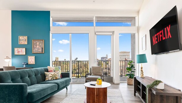 En stue med en tealgrøn sofa, et sofabord, et fjernsyn og en balkon med udsigt.