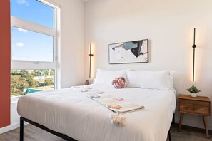 A bedroom with a large bed, a nightstand, a wall-mounted lamp, and a window with a view. - Skyline Luxe, Downtown LA, Epic Rooftop Views, Walk to Dodger Stadium (Los Angeles)