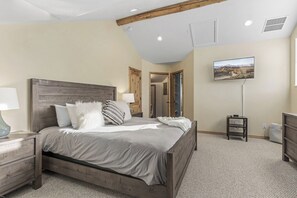 Un dormitorio con cama de madera, mesitas de noche, televisor de pantalla plana y un pasillo que conduce a otra habitación.