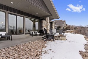 Une maison moderne dotée de grandes fenêtres, d’un espace extérieur aménagé et d’une cheminée en pierre.