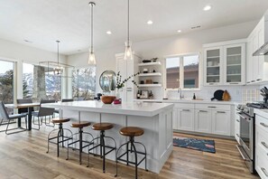 A modern kitchen with a large island, bar stools, and pendant lighting. - Nordic View Haven | Golf | Mtn View | Hot Tub (Eden)