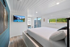 Ein Schlafzimmer mit Bett, einem an der Wand befestigten Fernseher, einem Fenster mit Aussicht und einer Tür zum Badezimmer.