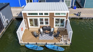 Una casa flotante con terraza, asientos al aire libre y dos kayaks.