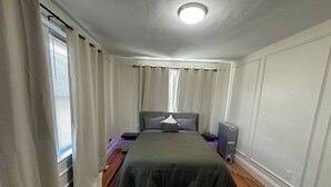 A bedroom with a bed, a radiator, a window with curtains, and a patterned rug. - Fully private 1bed apt brookline (Brookline)