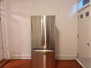 A stainless steel refrigerator in a corner of a room with wooden flooring and white walls. - Enjoyable 1-bedroom in a townhome with AC in vibrant Washington (Washington)