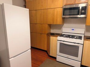 A kitchen with a white refrigerator, a microwave, a stove, and wooden cabinets. - Enjoyable 1-bedroom in a townhome with AC in vibrant Washington (Washington)