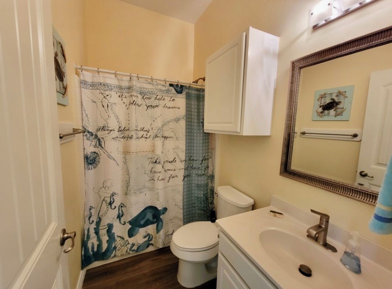 Een badkamer met douchegordijn met een kaartmotief, een toilet, een wastafel met spiegel en een handdoekrek.