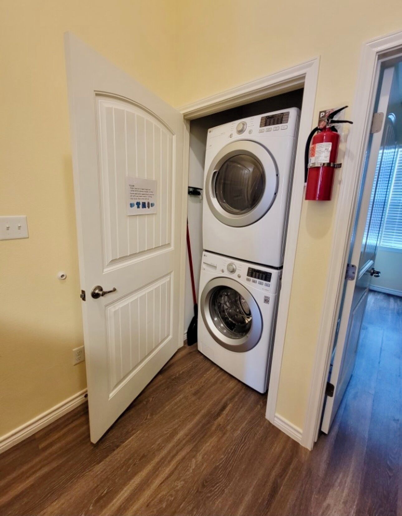 A laundry room with two stacked front-loading washing machines, a fire extinguisher mounted on the wall, and a door leading to another room.