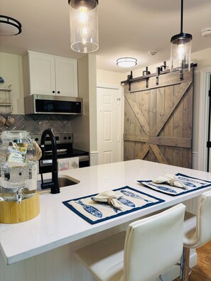 A kitchen with a central island, white cabinetry, a microwave, and a wooden barn-style door.