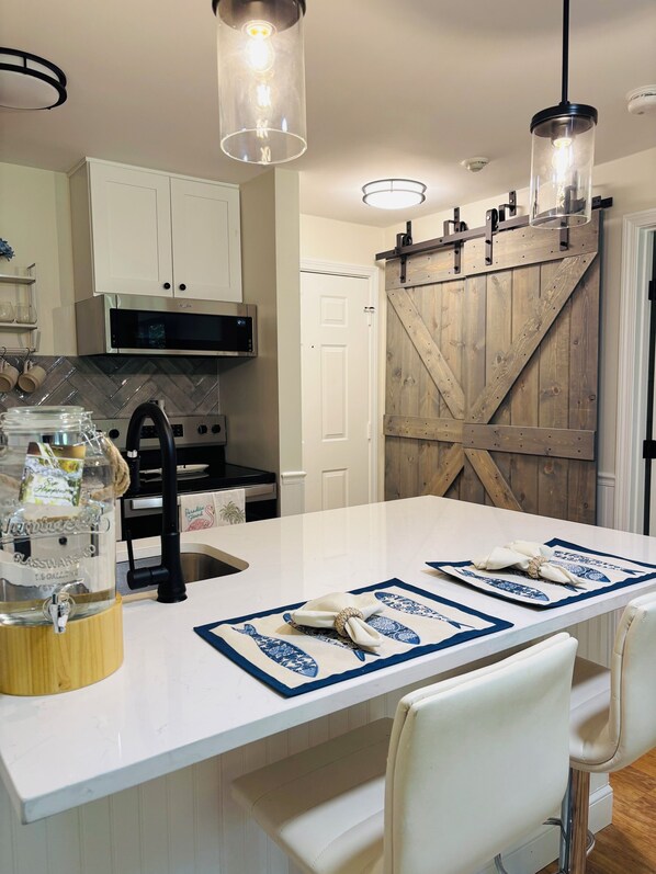 A kitchen with a central island, white cabinetry, a microwave, and a wooden barn-style door.